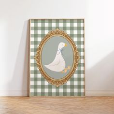 a white duck with a blue bow on its head in a gold frame against a green and white checkered wall