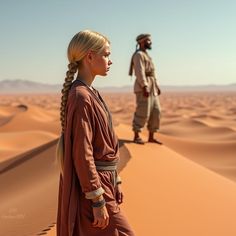 a man and woman standing in the desert with sand dunes behind them, looking at each other