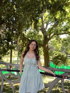 a woman in a blue dress standing on a wooden fence with trees and grass behind her