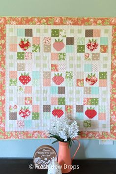 a vase filled with flowers sitting next to a quilted wall hanging on a wall