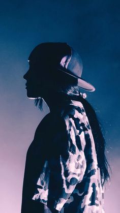 a man with long hair wearing a fedora and standing in front of a blue sky