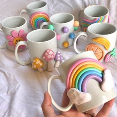 a hand holding a coffee cup with rainbow decorations on it and many mugs in the background