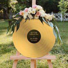 a gold record with flowers on it sitting in the grass next to a wooden easel