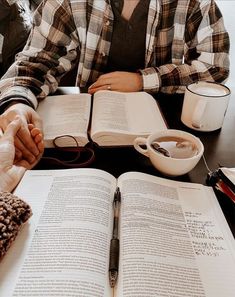 two people sitting at a table with an open book in front of them and coffee cups