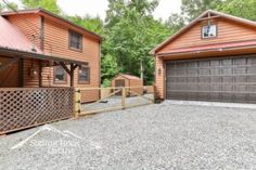 two brown garages sitting next to each other on top of a gravel lot in front of trees