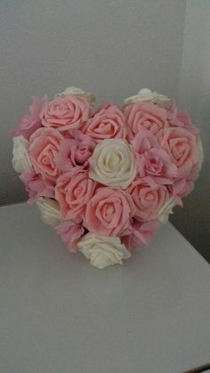 a bouquet of pink and white roses in the shape of a heart on a table