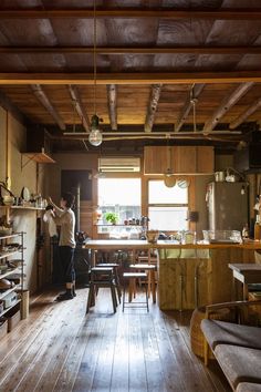 two people standing in a kitchen next to a table with chairs and stools on it