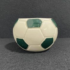 a white and green soccer ball sitting on top of a gray table next to a black wall