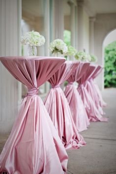 the tables are lined up with pink cloth draped over them and white flowers in vases