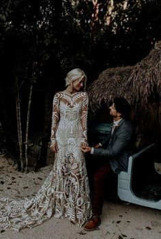 a man and woman standing next to each other in front of a car with thatched roof