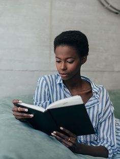 a woman reading a book while sitting on a bed