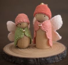 two small wooden angel figurines sitting on top of a piece of wood