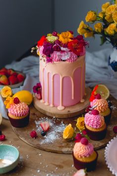 there is a pink cake with flowers on the top and cupcakes around it