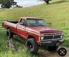 an old red pickup truck is parked on the side of a dirt road near a fence