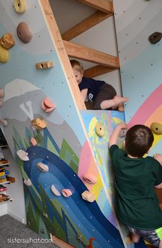 two young boys climbing up the side of a wall with colorful rocks and paper on it