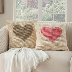 two pillows with hearts on them sitting on a couch in front of a large window