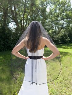 the back of a woman wearing a white dress with a veil over her head, standing in a field