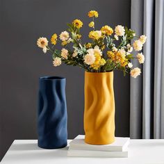 two vases with yellow and blue flowers in them sitting on a table next to each other