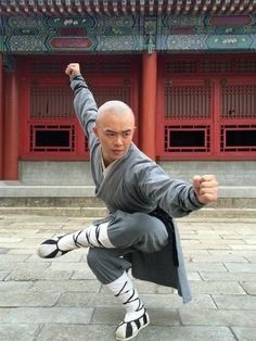 a man is doing karate in front of a building with red pillars and doors behind him