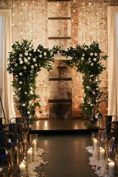 an indoor ceremony with candles and flowers on the aisle, surrounded by white roses and greenery