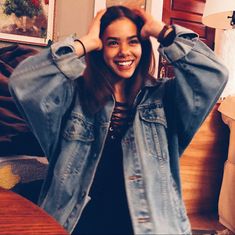 a woman is smiling and holding her hair in front of her face while wearing a jean jacket