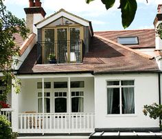 a large white house with a deck in front of it and lots of windows on the roof