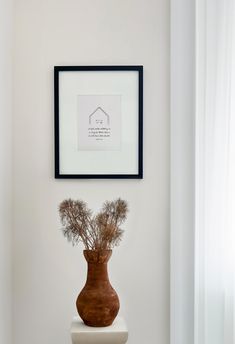 a vase with dried flowers in it sitting on top of a white toilet seat next to a framed picture