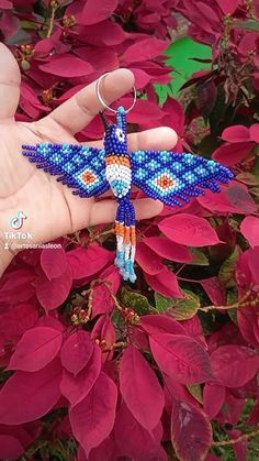 a hand holding a beaded dragon keychain in front of purple flowers with red leaves