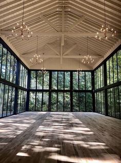 an empty room with lots of windows and wood flooring in the center is lit by chandeliers that are hanging from the ceiling