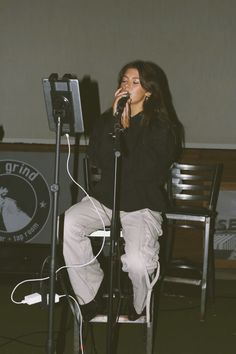 a woman singing into a microphone while sitting on a chair in front of a microphone