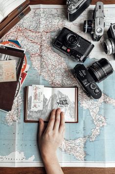 a person is holding an open book on top of a map with cameras and books nearby