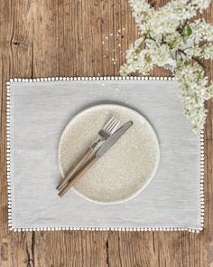 a white plate topped with a fork and knife on top of a wooden table next to flowers