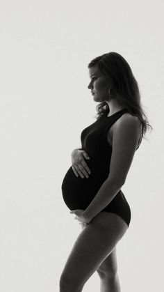 a pregnant woman in a black bodysuit poses for the camera with her hands on her hips