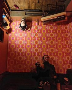 a man sitting on the floor in front of a wall with an orange and pink pattern