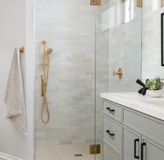 a bathroom with white and gold fixtures, marble counter tops, and tile shower walls