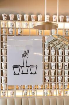 a bunch of cups that are sitting on a shelf in front of a sign with a plant