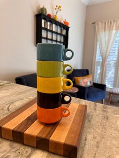 three coffee mugs stacked on top of each other sitting on a cutting board in front of a window