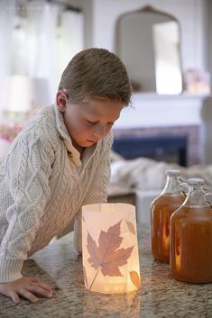 a young boy looking at a paper lantern with a maple leaf on it and two jars next to it