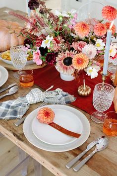 a wooden table topped with white plates covered in flowers and candles next to pumpkins