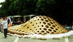 a large wooden structure sitting on the side of a road next to people and trees