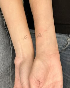 two people holding hands with small tattoos on their wrist and the other one has a heart