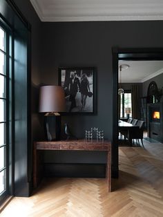 a room with black walls and wood flooring has a lamp on the end table