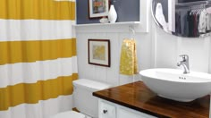 a bathroom with yellow and white striped shower curtain, sink and wood countertop in front of the mirror