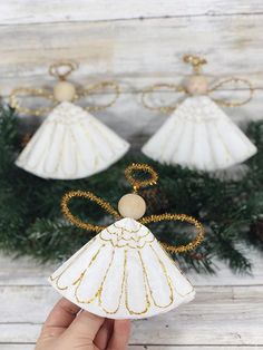 a hand holding an angel ornament in front of a christmas wreath and pine branches