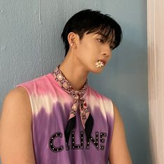 a young man wearing a tie dye shirt and flower in his mouth, standing against a blue wall