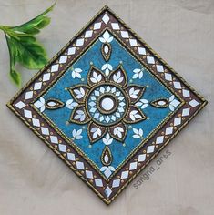 a blue and brown decorative tile sitting on top of a white table next to a green plant