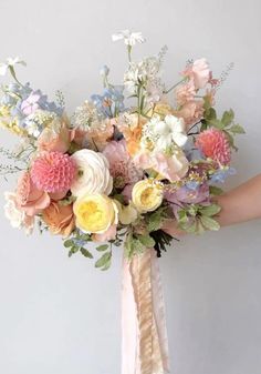 a bridal bouquet with pink, yellow and white flowers is held by a woman's hand