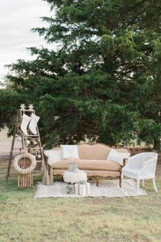 a couch and chair sitting on top of a grass covered field next to a tree