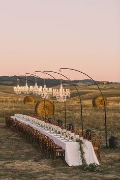 a long table is set up in the middle of an open field with chandeliers