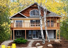 a house in the woods surrounded by trees and rocks with yellow chairs on the front lawn